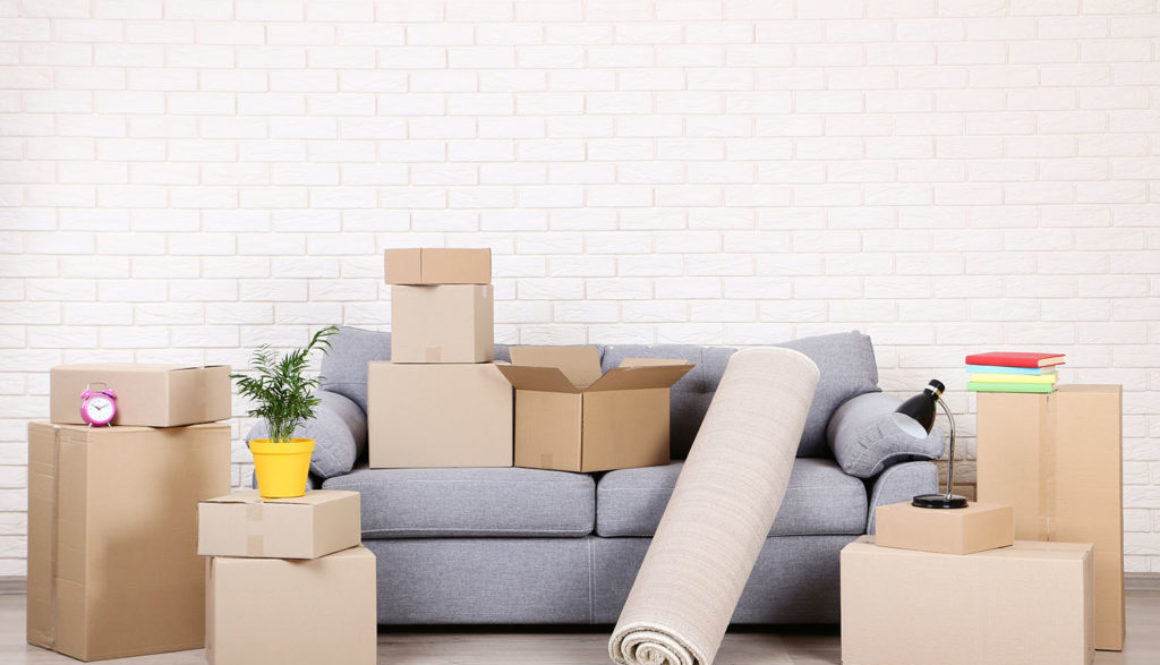 Cardboard boxes with household stuff and grey sofa on brick wall background
